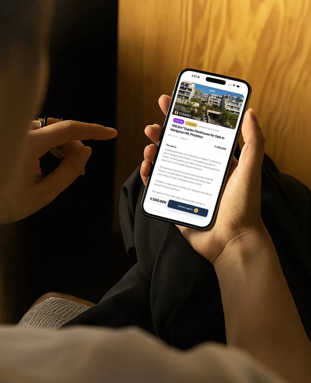 A hand holding a phone with the Domino app open on a penthouse listing and Contact agent