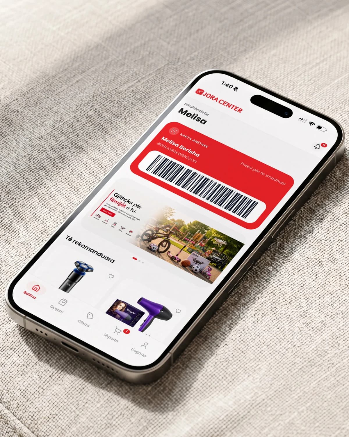 Ein iPhone auf strukturiertem Stoff zeigt den Startbildschirm der App von Jora Center mit einer Muster-Kundenkarte, Barcode und empfohlenen Produkten