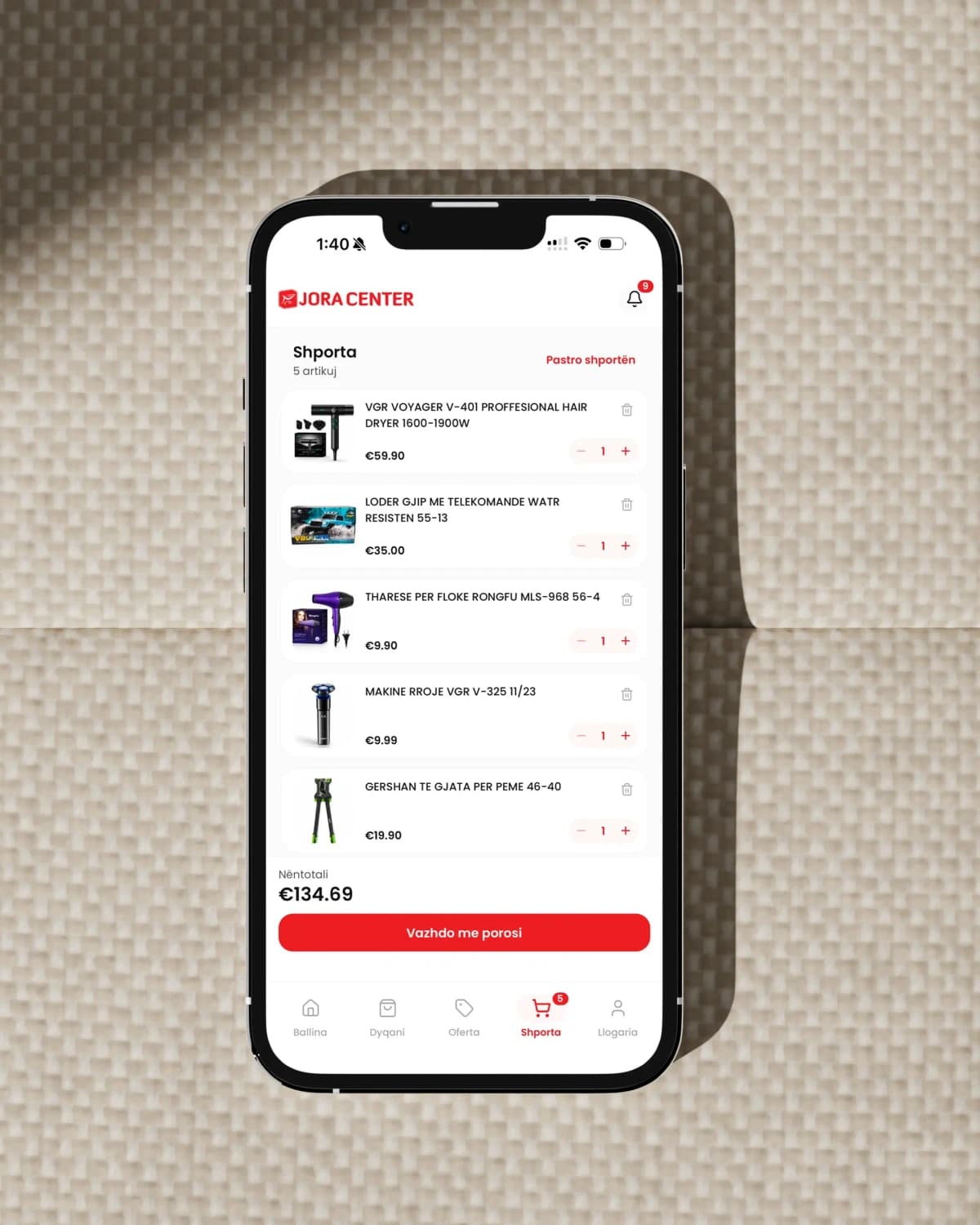 Ein iPhone auf gewebtem Stoff zeigt den Warenkorb der App von Jora Center mit fünf Produkten, Mengensteuerung und der Schaltfläche zum Bestellen
