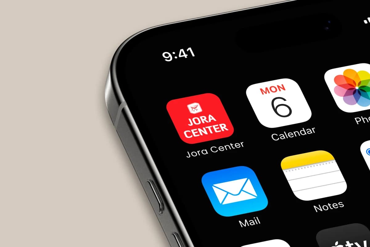 Nahaufnahme eines iPhone-Startbildschirms mit dem roten App-Icon von Jora Center neben Kalender, Mail und Notizen, vor beigem Hintergrund