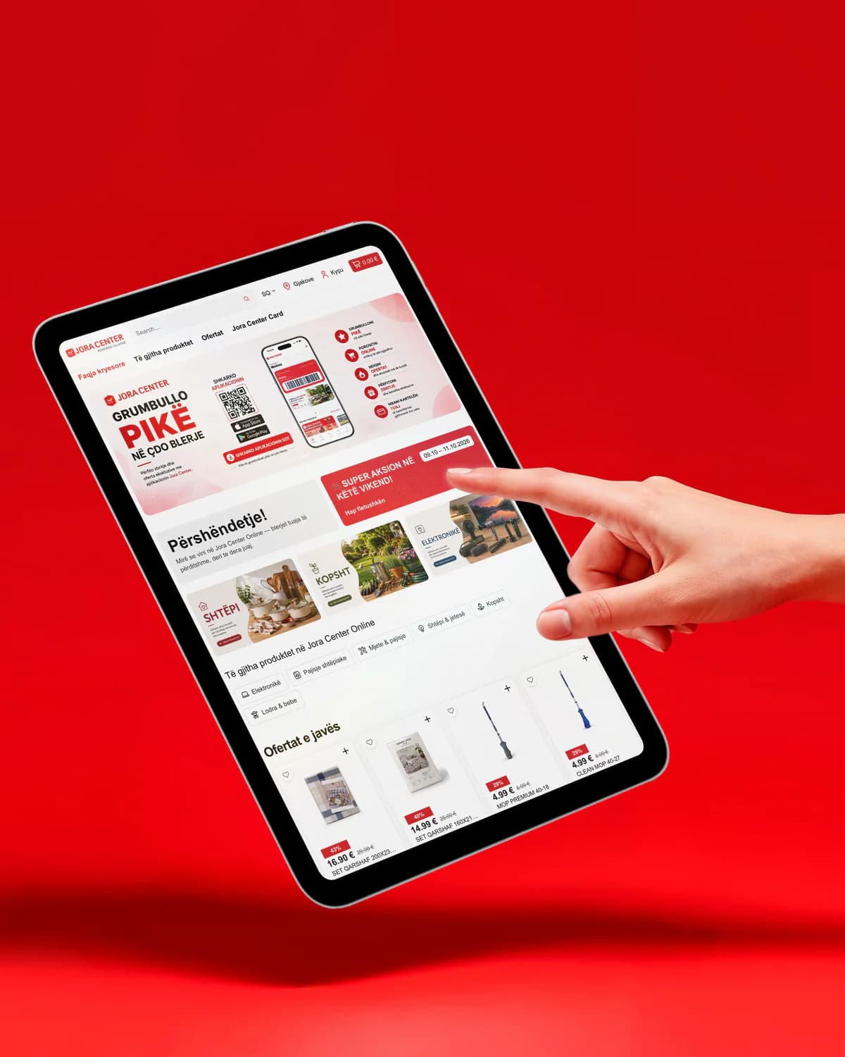 Eine Hand greift vor rotem Hintergrund nach einem Tablet mit der Startseite des Onlineshops von Jora Center