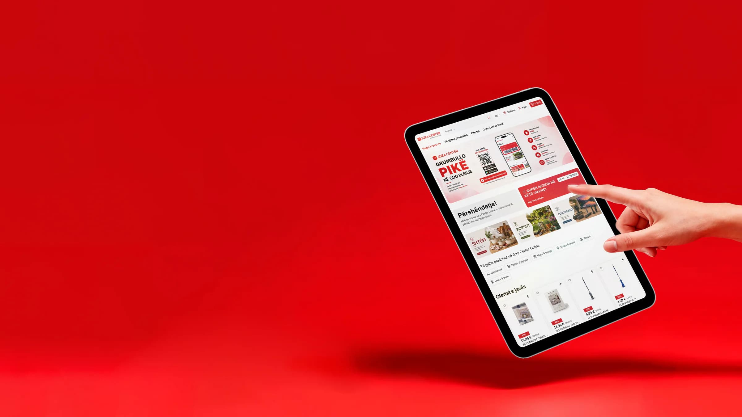 Eine Hand greift vor rotem Hintergrund nach einem Tablet mit der Startseite des Onlineshops von Jora Center