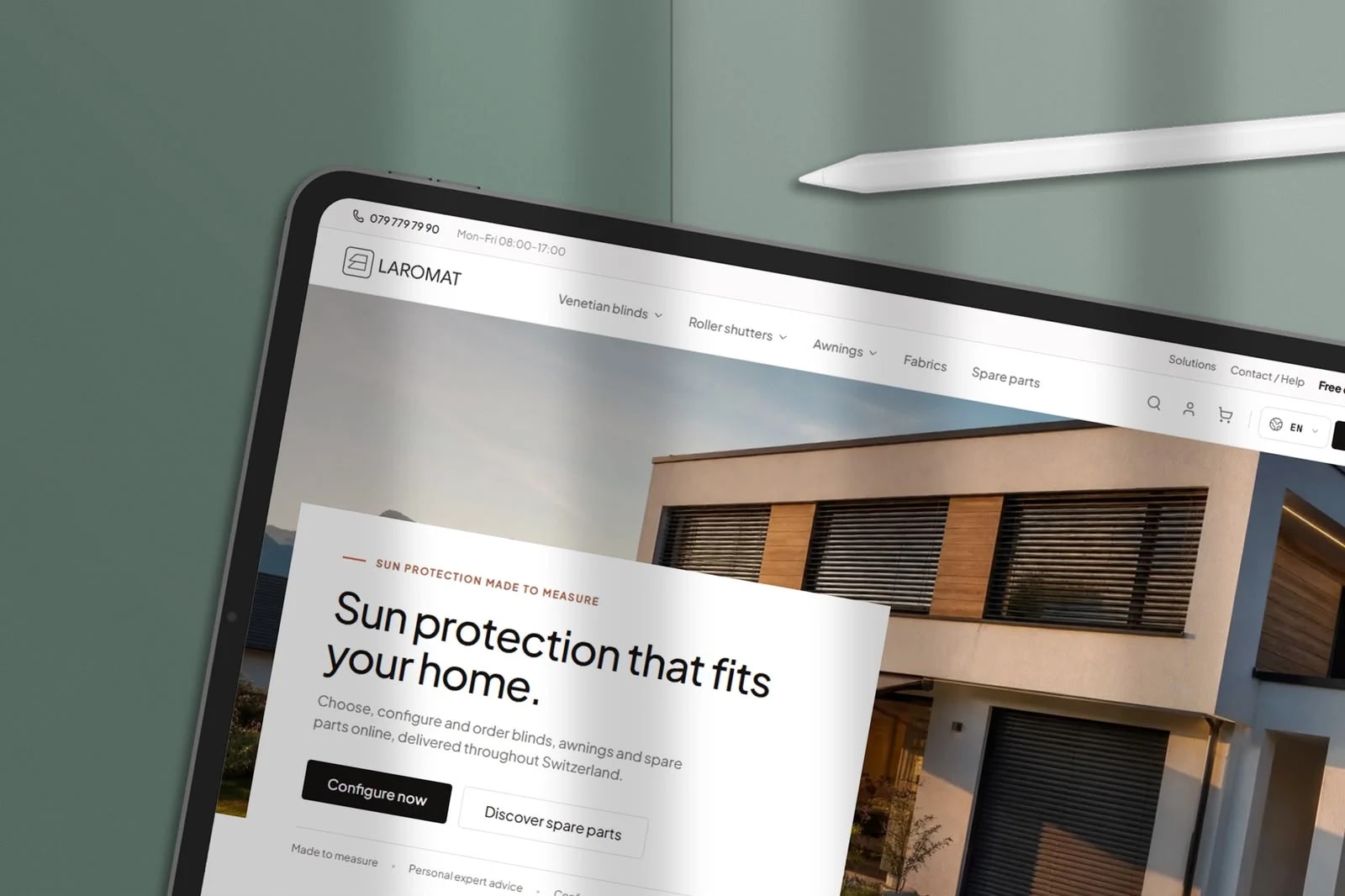 Ein Tablet mit Stift auf salbeigrünem Grund, darauf die Startseite von Laromat: ein Haus mit Lamellenstoren und die Überschrift «Sun protection that fits your home»
