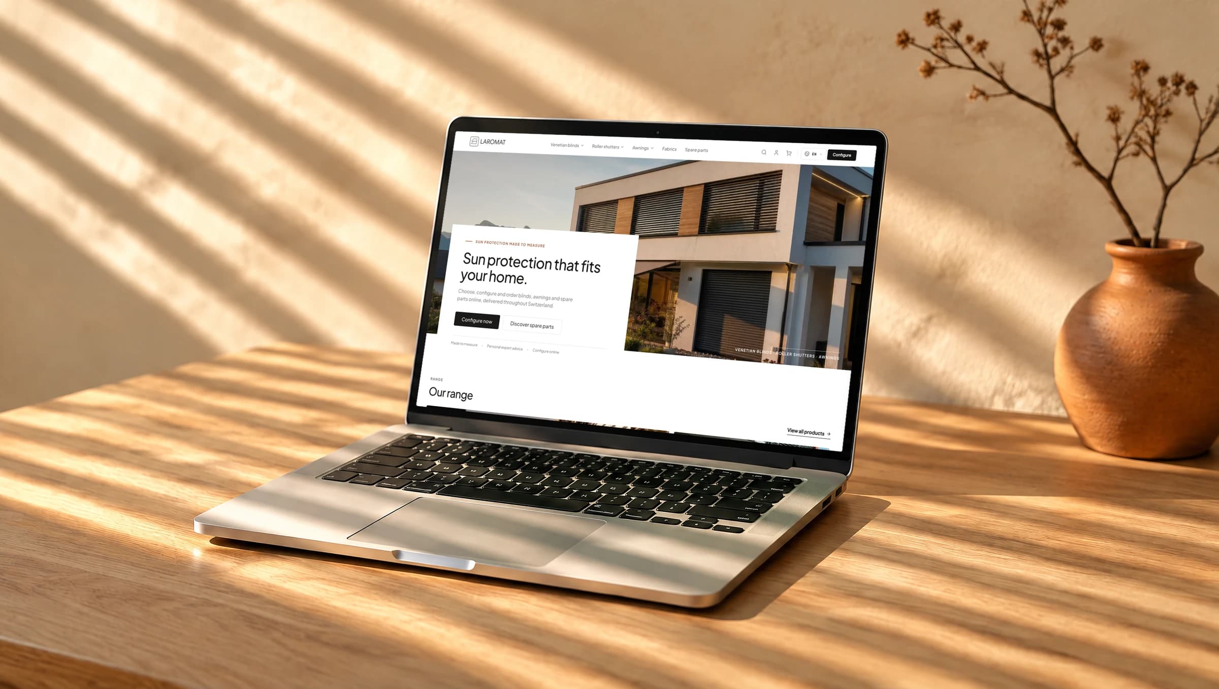 Ein Laptop auf einem Eichentisch in tief stehender Sonne mit Lamellenschatten, darauf die Startseite von Laromat: ein Haus mit Lamellenstoren und die Überschrift «Sun protection that fits your home»