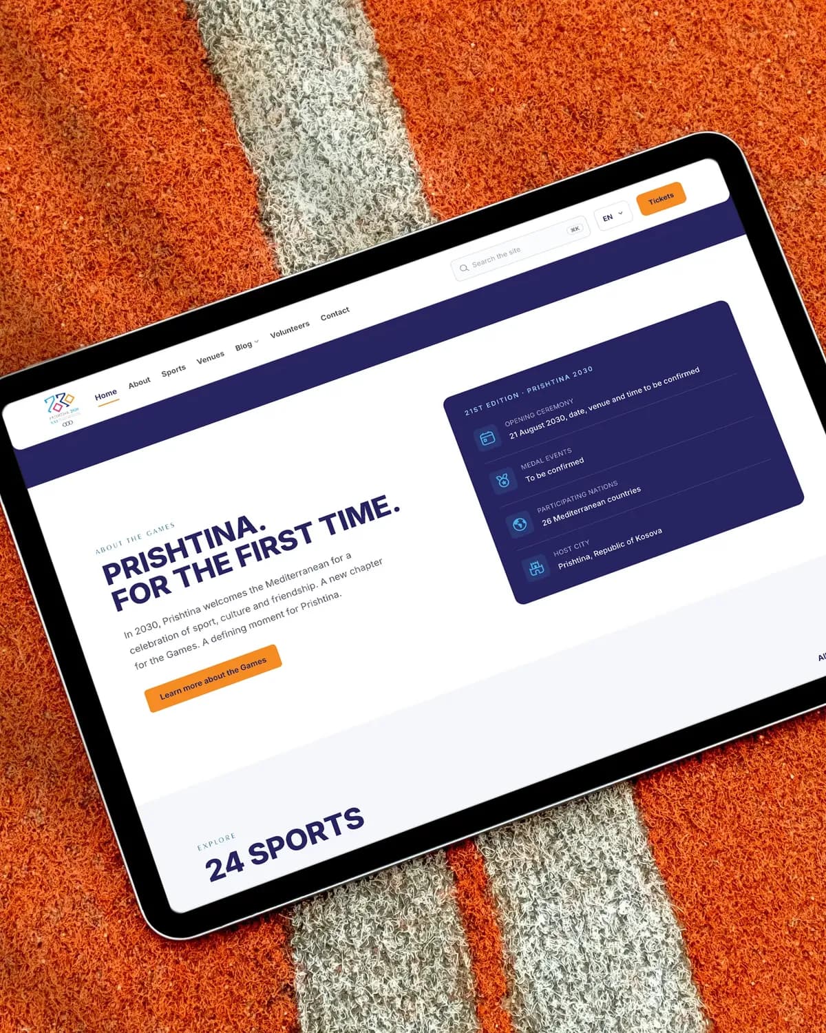 A tablet lying on an orange running track, showing the Prishtina 2030 home page: Prishtina. For the first time.