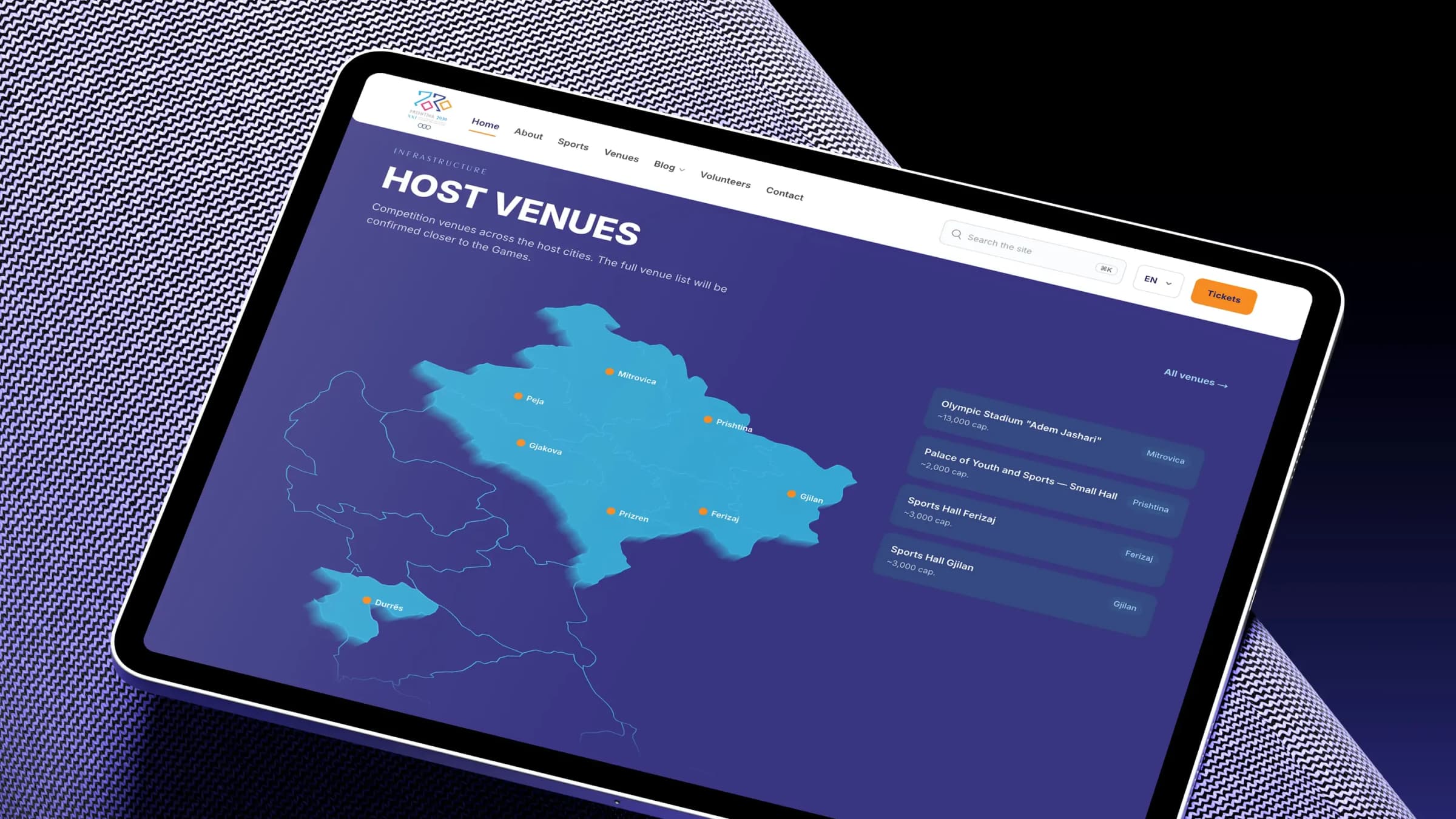 A tablet on a woven purple surface, showing the Prishtina 2030 host venues page with a map of Kosovo and the confirmed venues